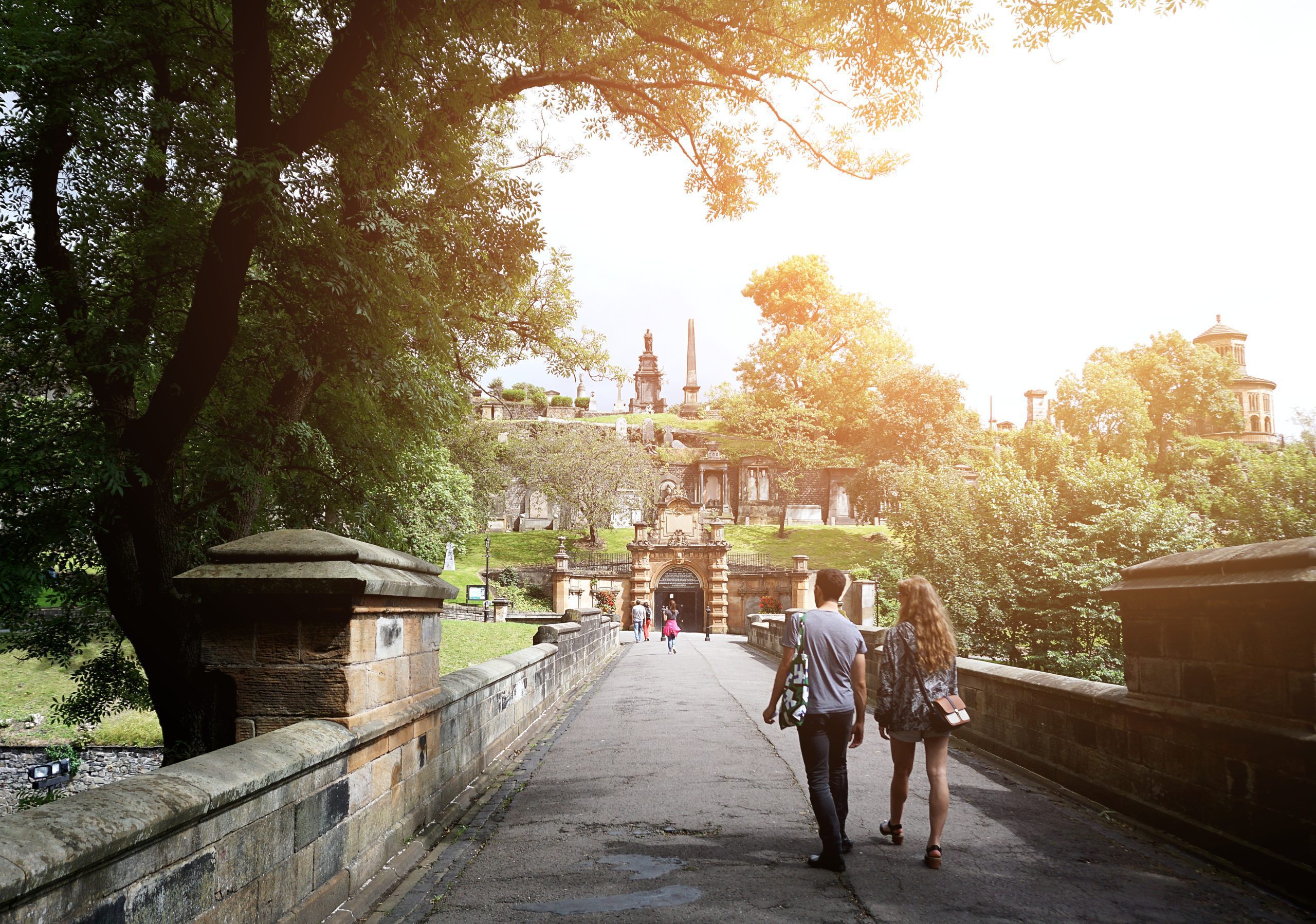 A man and a woman walking across a tree lined bridge in Glasgow, Scotland